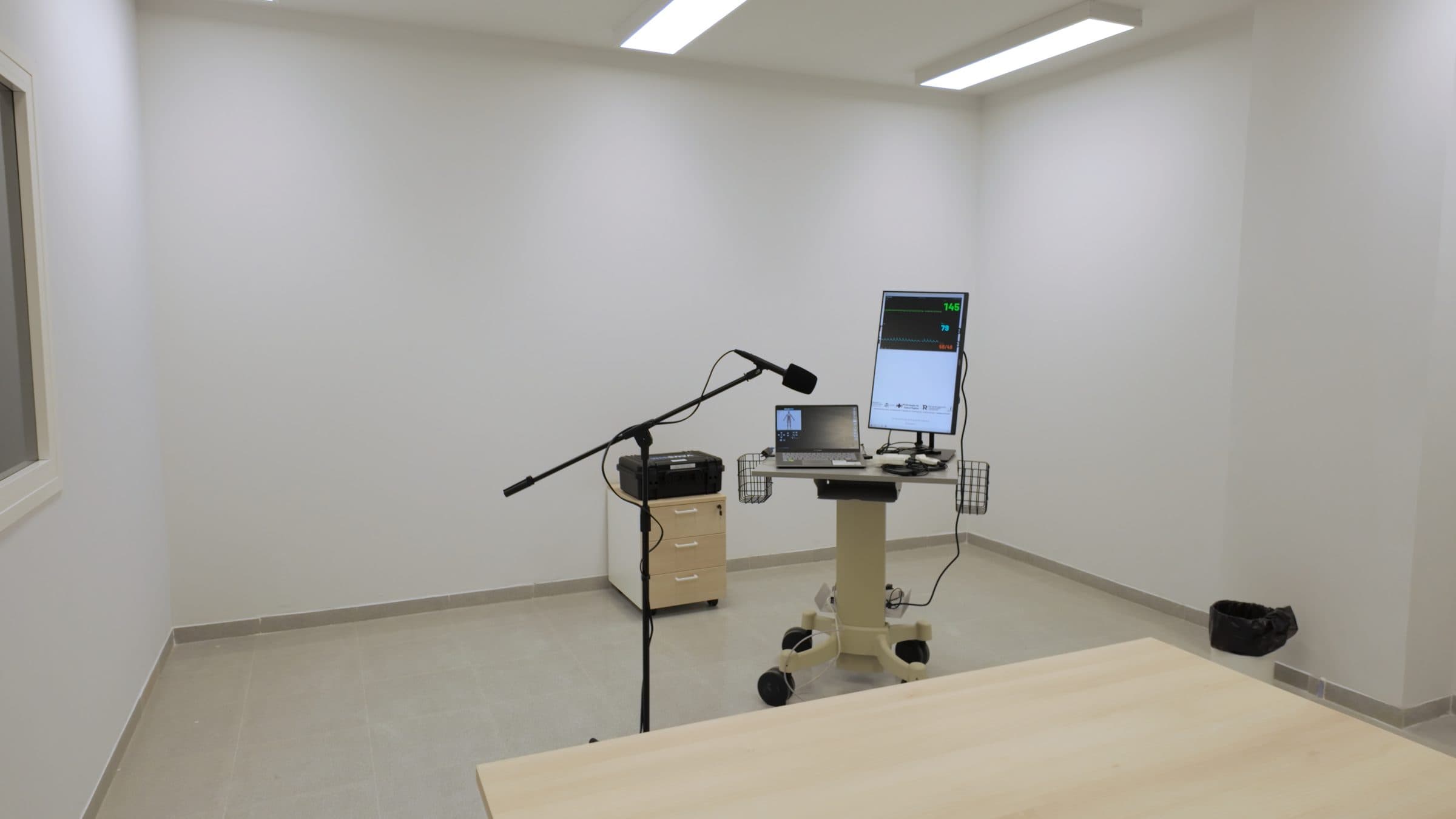 Espacio de práctica del aula con el carro clínico, el monitor en vertical y el micrófono orientado hacia la zona de trabajo.