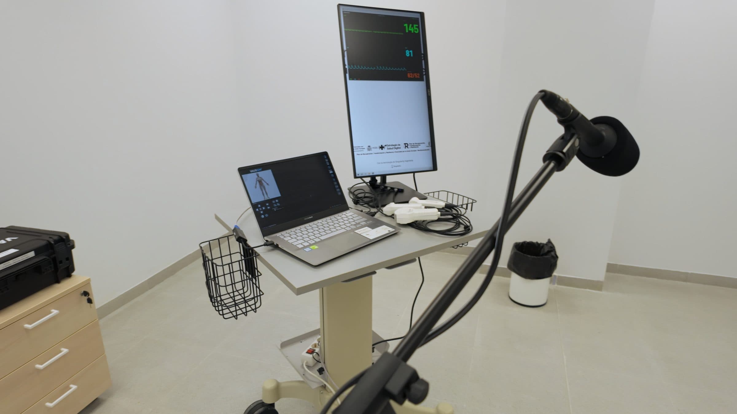 Estación de simulación con portátil del simulador de ecografía, monitor de constantes en vertical y micrófono de ambiente en primer plano.